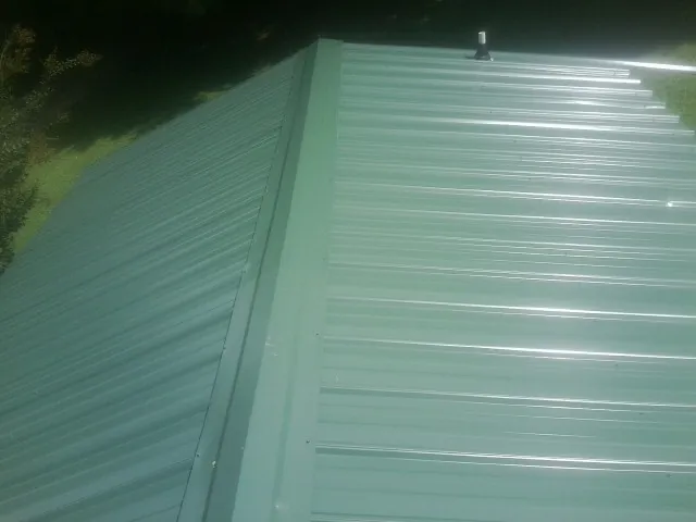 New green metal panels meeting at the ridge of a roof — Flat Roof Repair work by our crew in Unionville