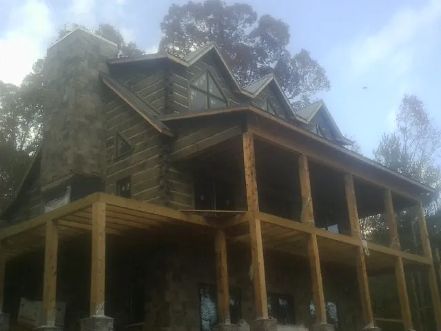 Stone chimney and dormers on a large log home with a timber porch in Unionville
